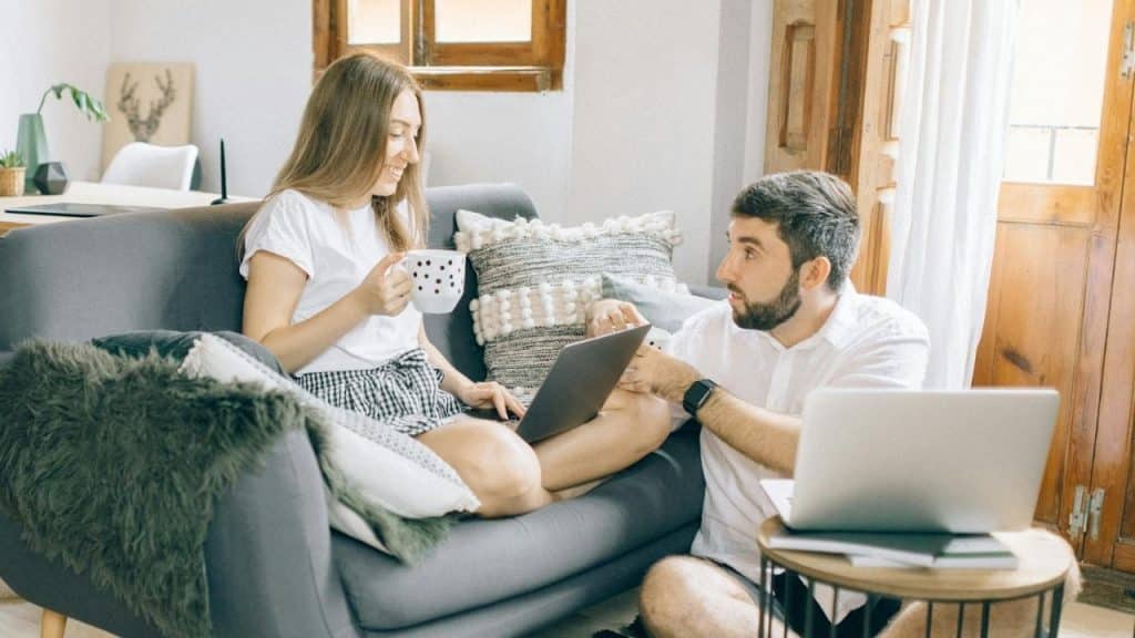 A woman on a sofa holds a mug while a man sits on the floor.