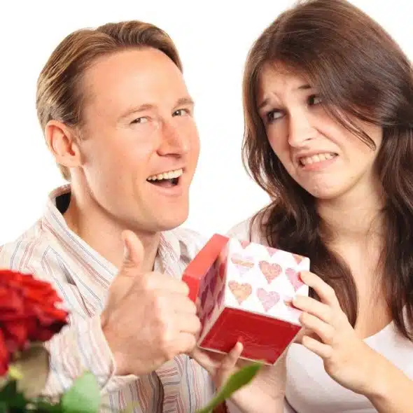 A man gives a thumbs up while a woman holds a heart-patterned gift box and grimaces.