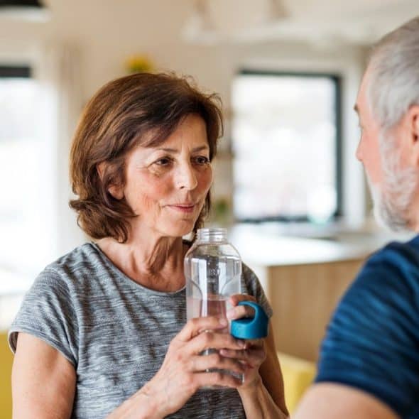 A woman drinking water from a bottle while her husband looks at her.