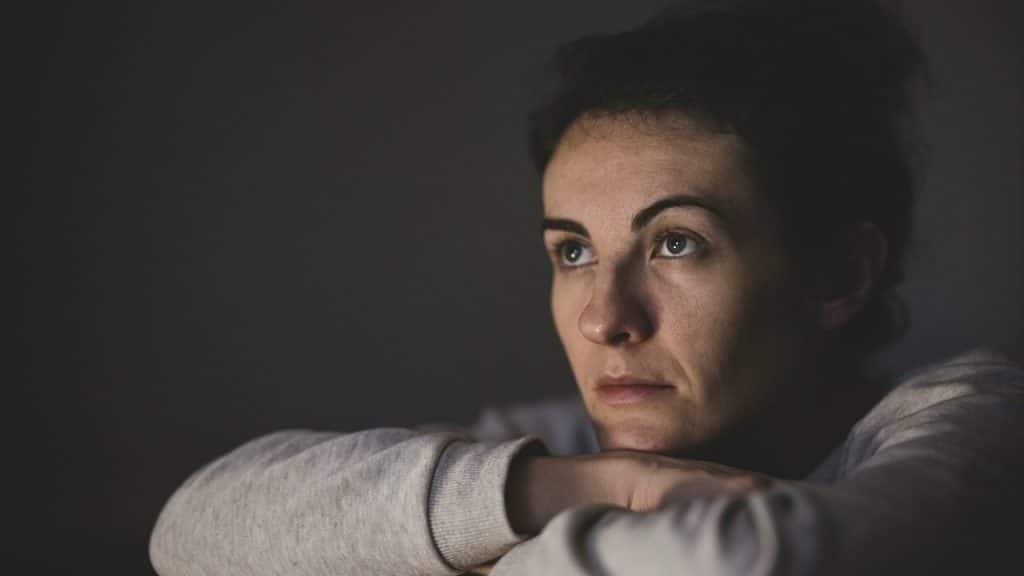 A woman rests her chin on her crossed arms, looking off into the distance with a somber and pensive expression.