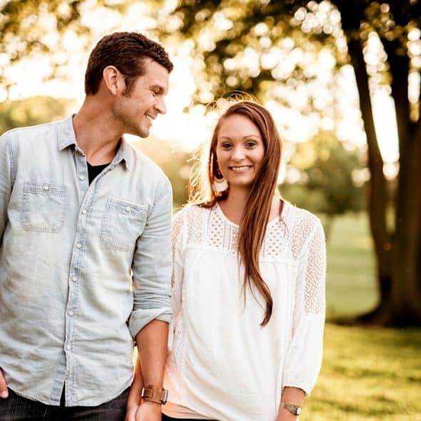 A smiling couple holding hands and walking through a park.