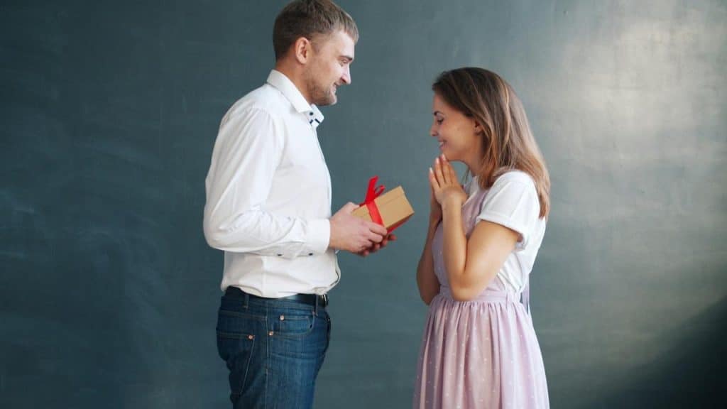 A man gives a woman a gift with surprised joy.