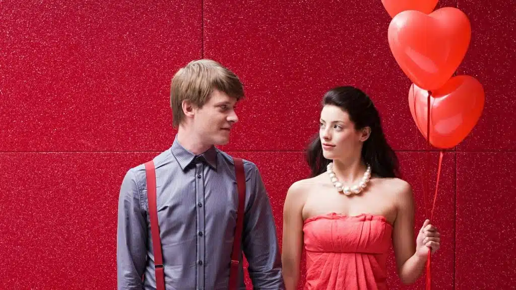 Woman holding heart balloons symbolizing romance and a man looking at her 