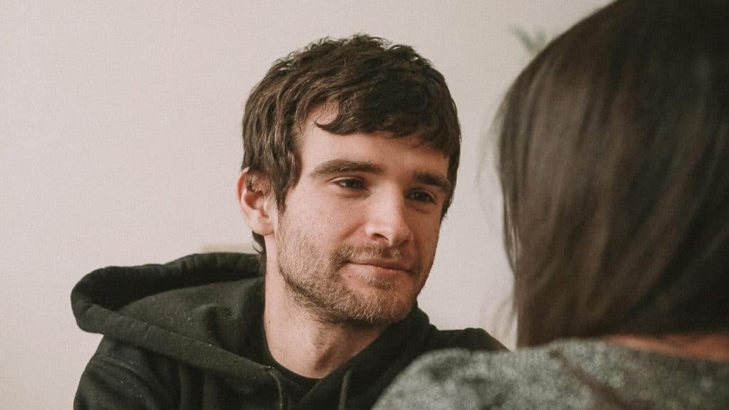 A man with a beard looks toward a person whose back is to the camera.