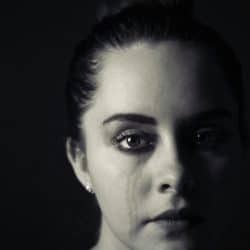 A woman is staring at the camera with tear stains on her cheek.