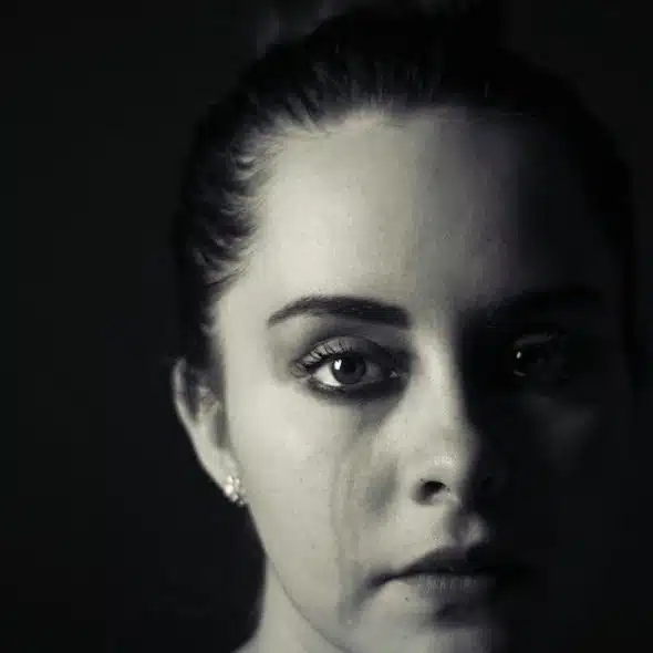 A woman is staring at the camera with tear stains on her cheek.