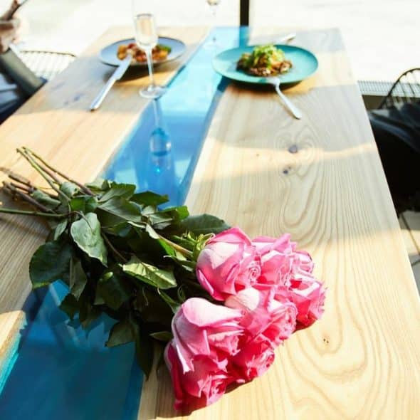 A bouquet of pink roses on a wooden table at a restaurant with two people using their phones.