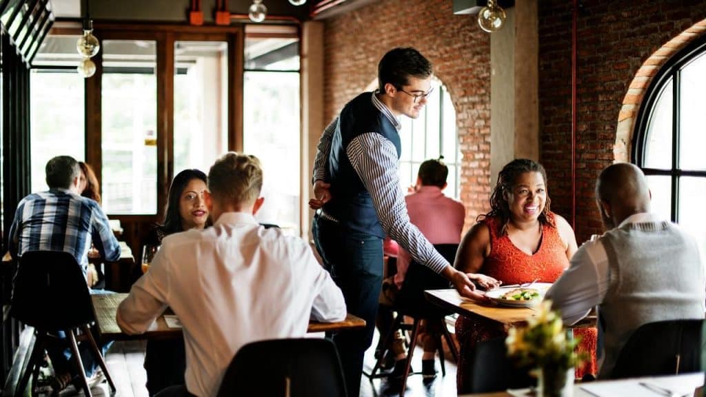 A waiter serving food to diners in a busy restaurant.