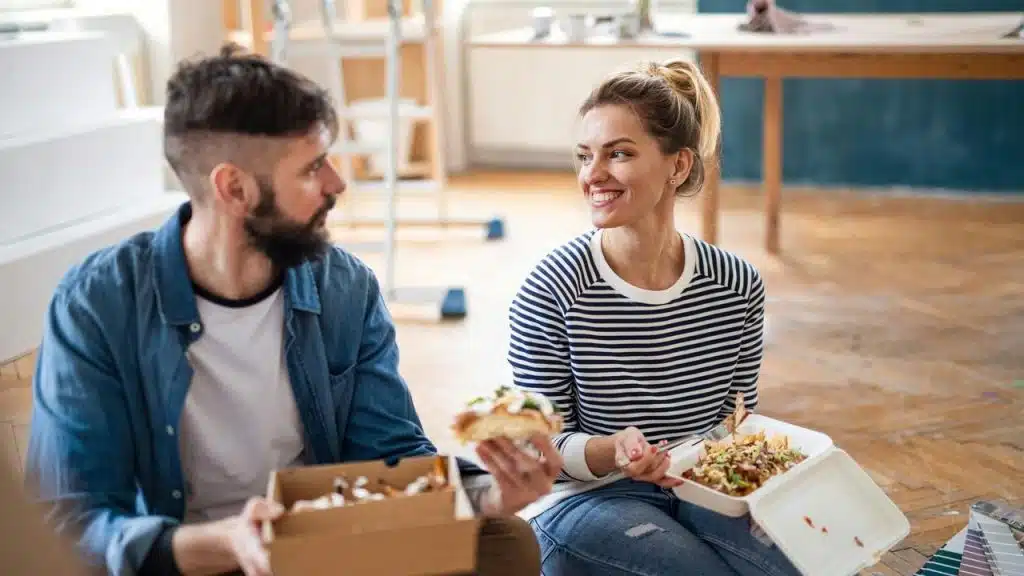 A couple sitting on the floor eating takeout during a home renovation.