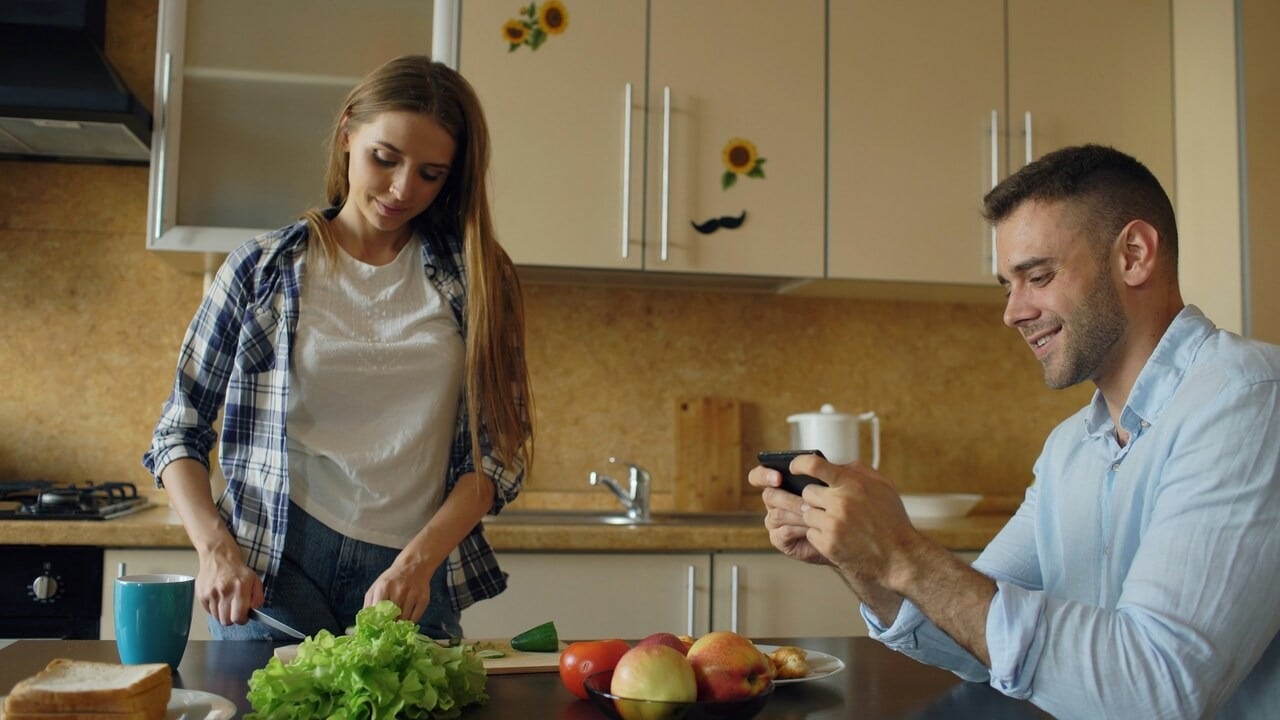 A woman does chores while her husband plays games