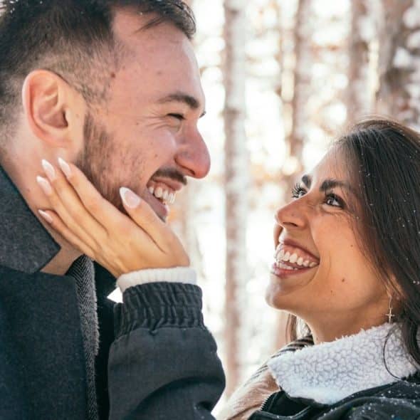 A woman smiling intensely and stroking a smiling man’s beard.