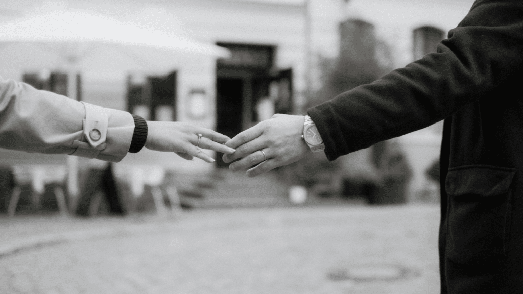 Two hands reach toward each other but do not touch in a black and white photo.