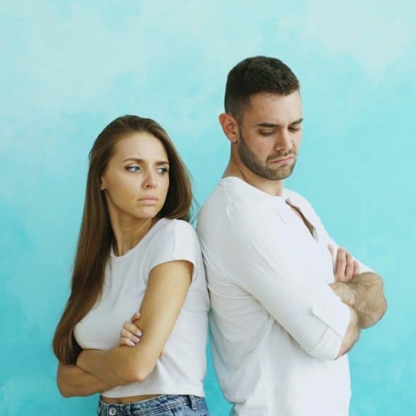 A couple standing back to back with arms crossed.