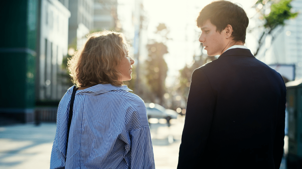 A man and woman walk down a sunny city street and look at each other.