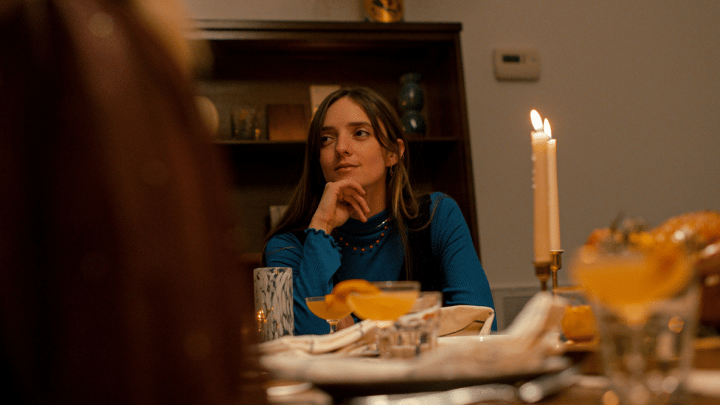A woman in a blue shirt sits at a dinner table with candles and drinks.