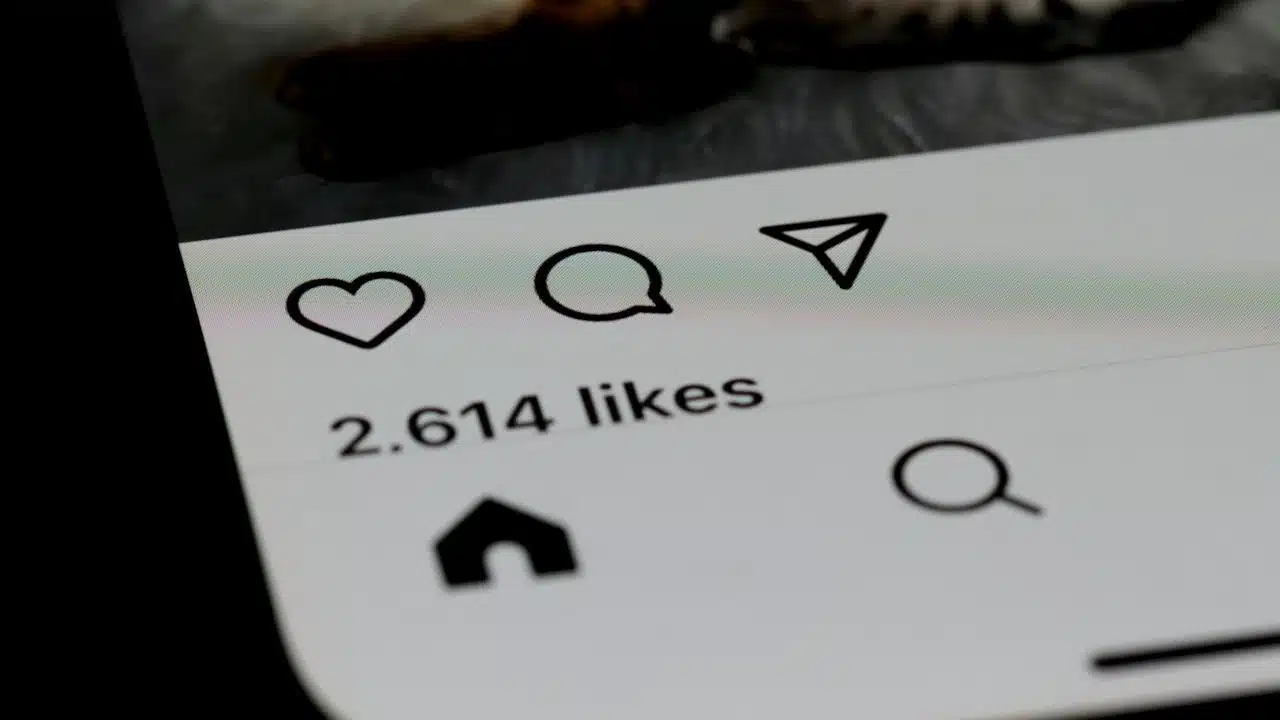 Close-up of a smartphone screen showing 2,614 likes and icons for like, comment, and share beneath an Instagram post.
