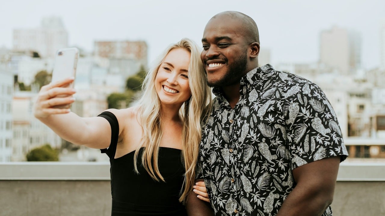 Diverse couple taking a selfie at a rooftop party.