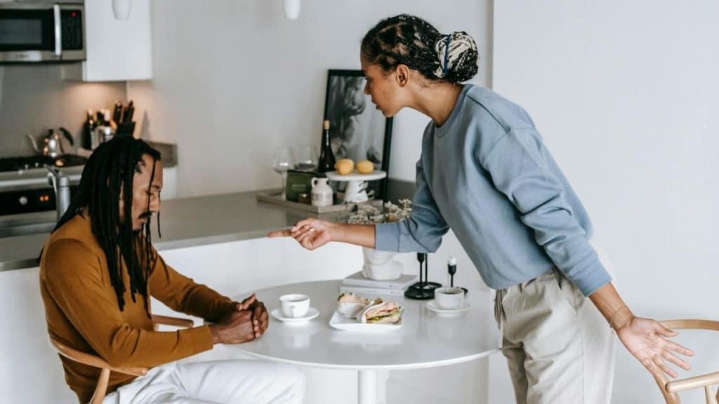 A woman stands and points a finger toward a seated man with his hands clasped.