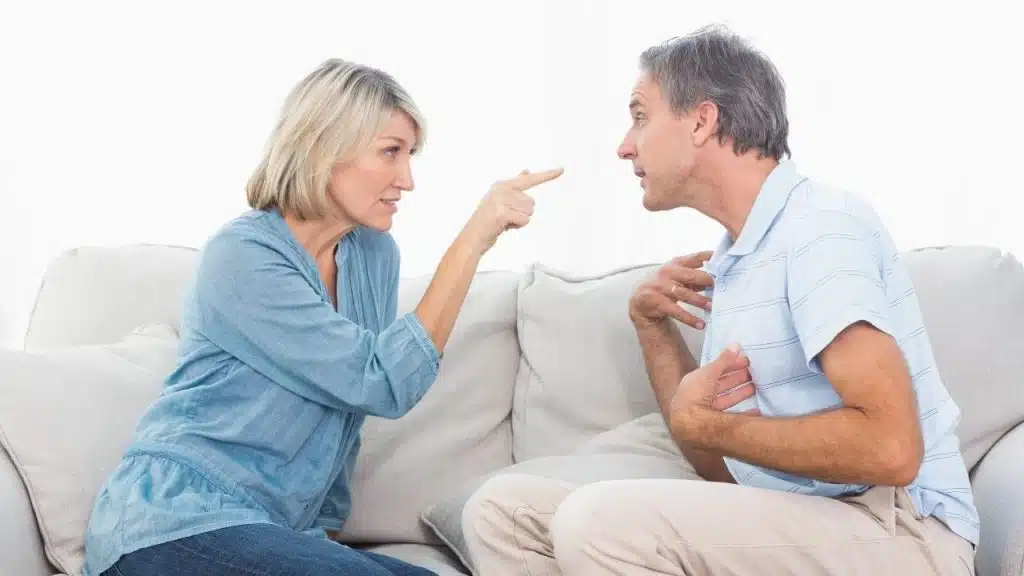 A man with glasses kisses the forehead of a woman resting her head on him.