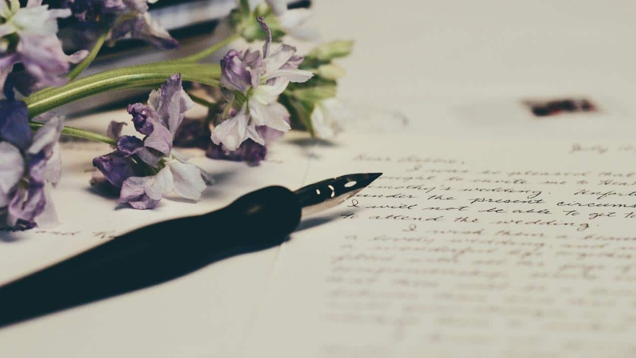 A fountain pen resting on handwritten paper beside purple flowers.
