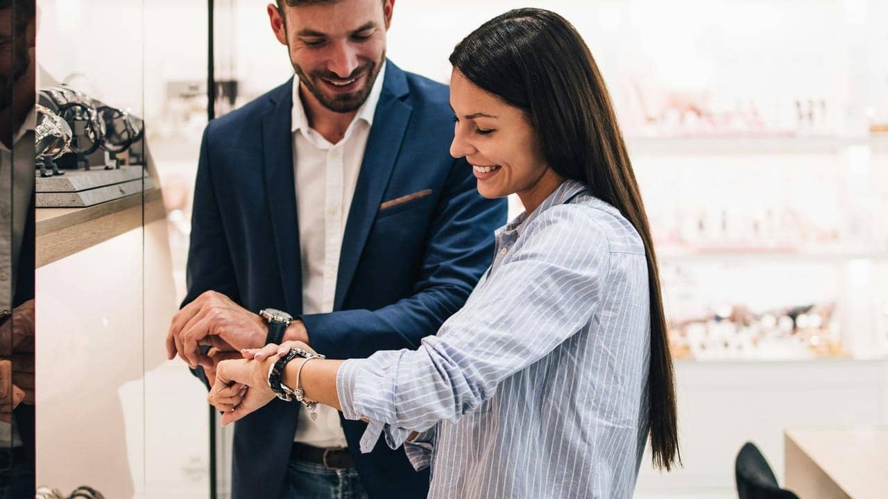 A couple smiling while trying on watches in a jewelry store.
