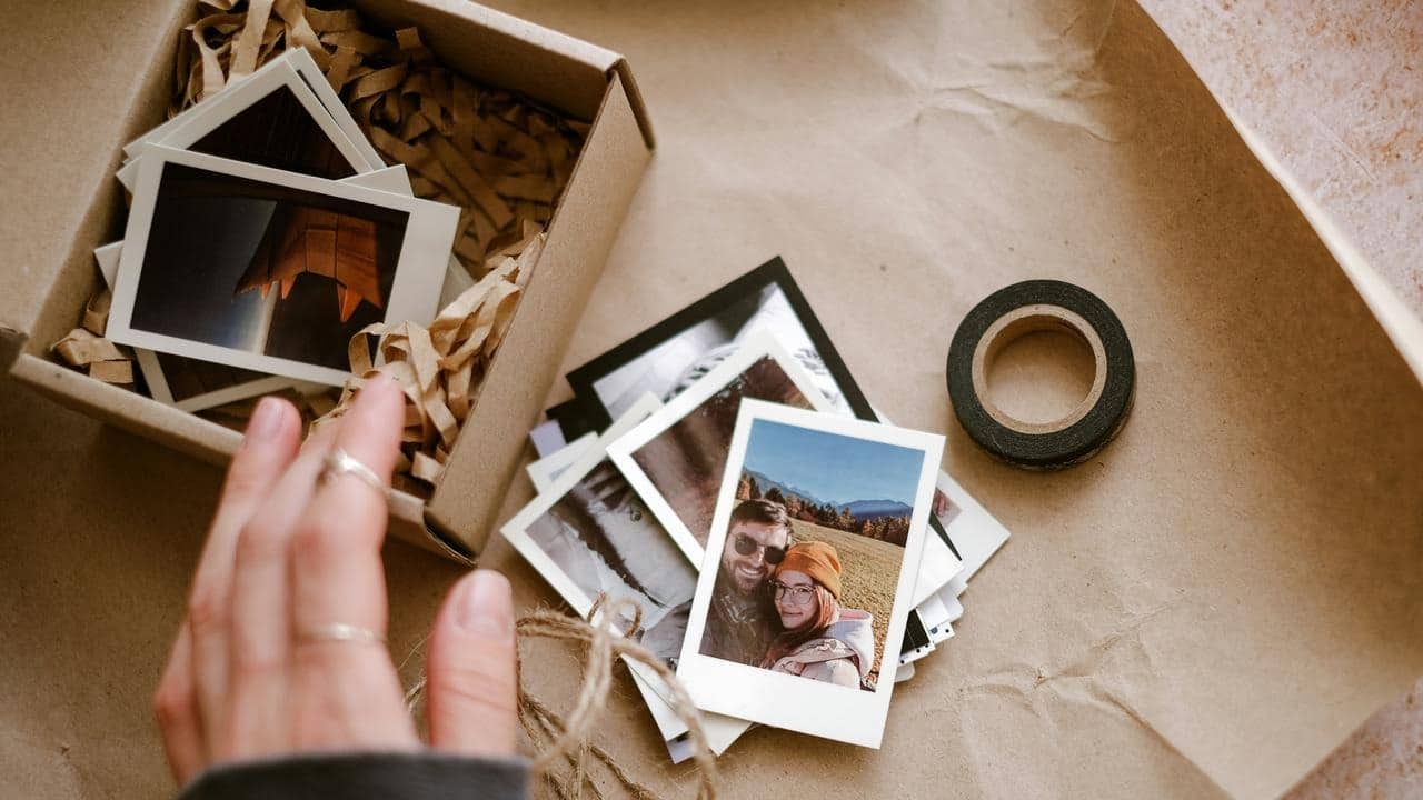 A hand sorting instant photos on brown paper next to a box and tape.