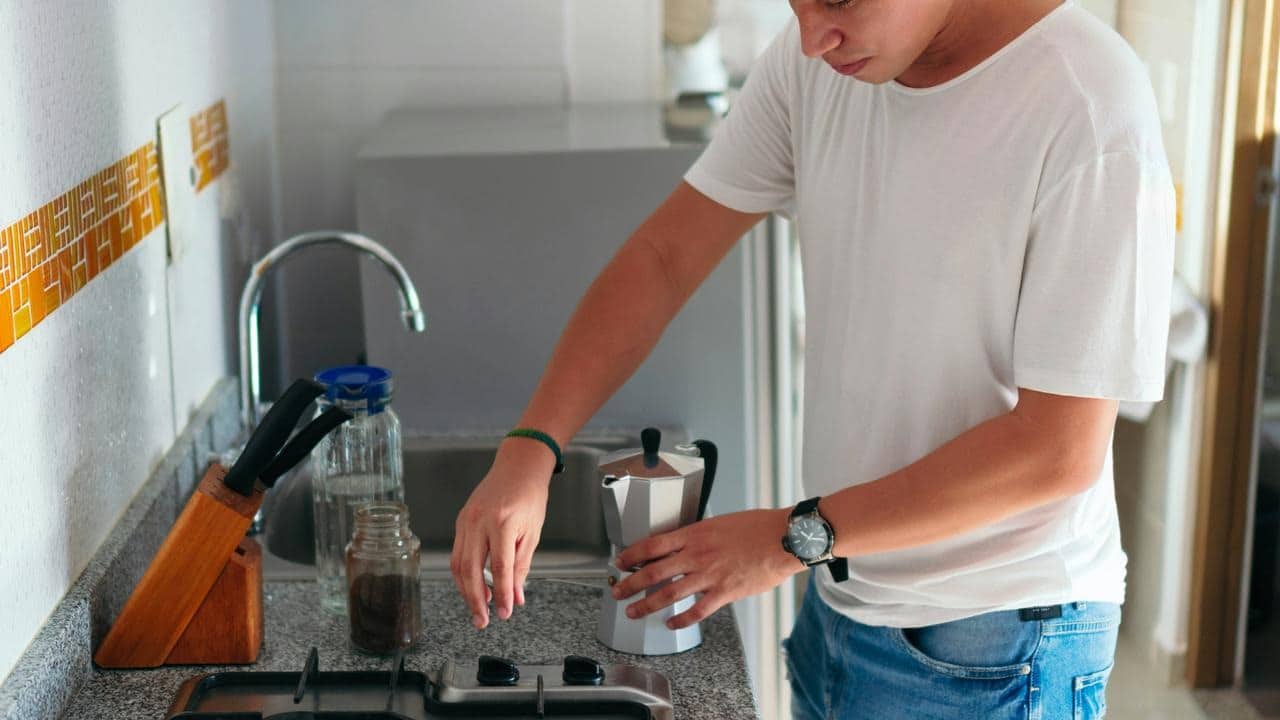 A man making coffee with a moka pot in a kitchen.
