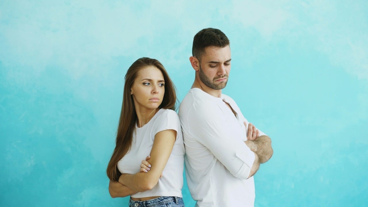 A couple standing back to back against a blue background.