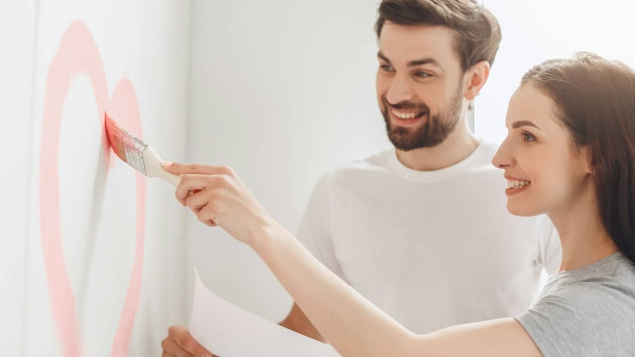 Young man and woman painting a heart on the apartment’s wall together.