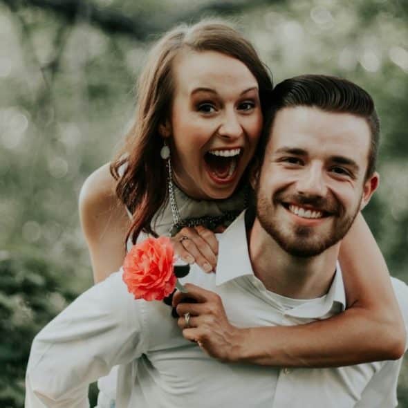 A woman holding a rose is riding on the back of a man.