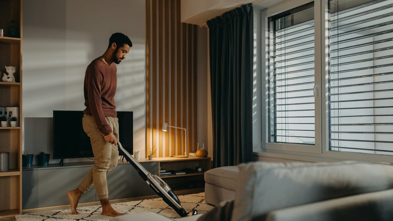 A man vacuum cleaning the carpet in the living room.