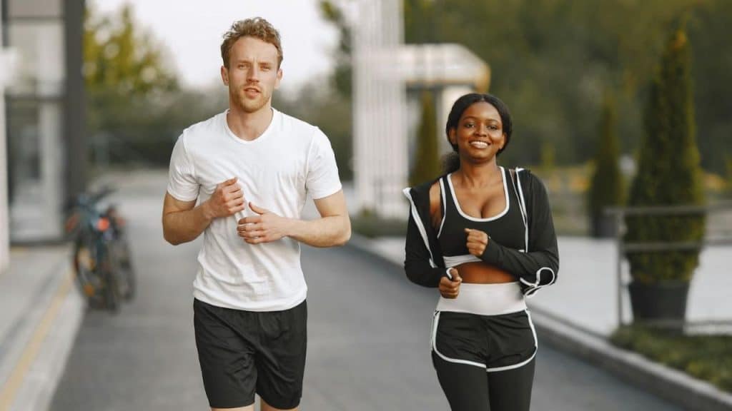 A man and woman in athletic wear jog together on a paved path outdoors.