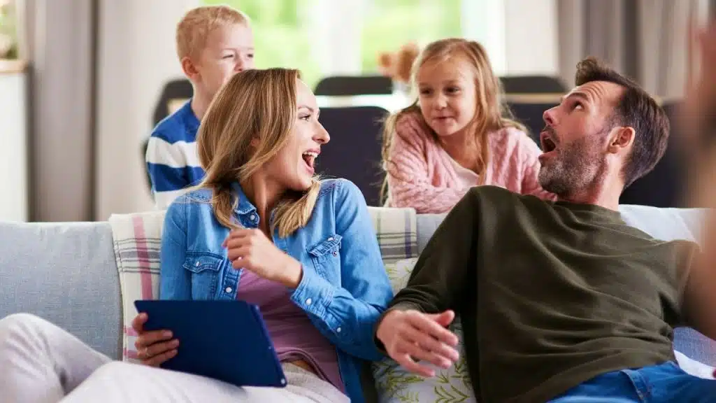 A man and woman sit on a sofa laughing together while two children look on.