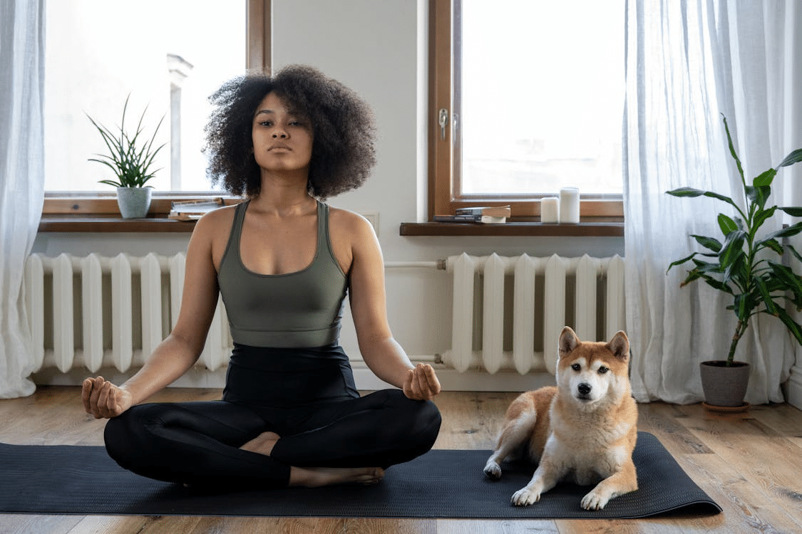 A woman doing yoga on a mat with a dog