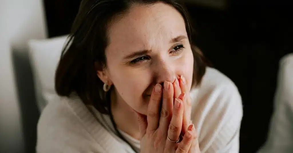 A woman holding her hands over her mouth with an emotional expression.