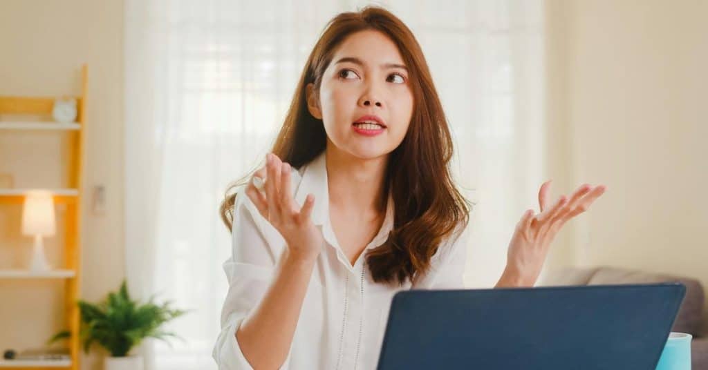 A woman gesturing while speaking in front of a laptop at home.