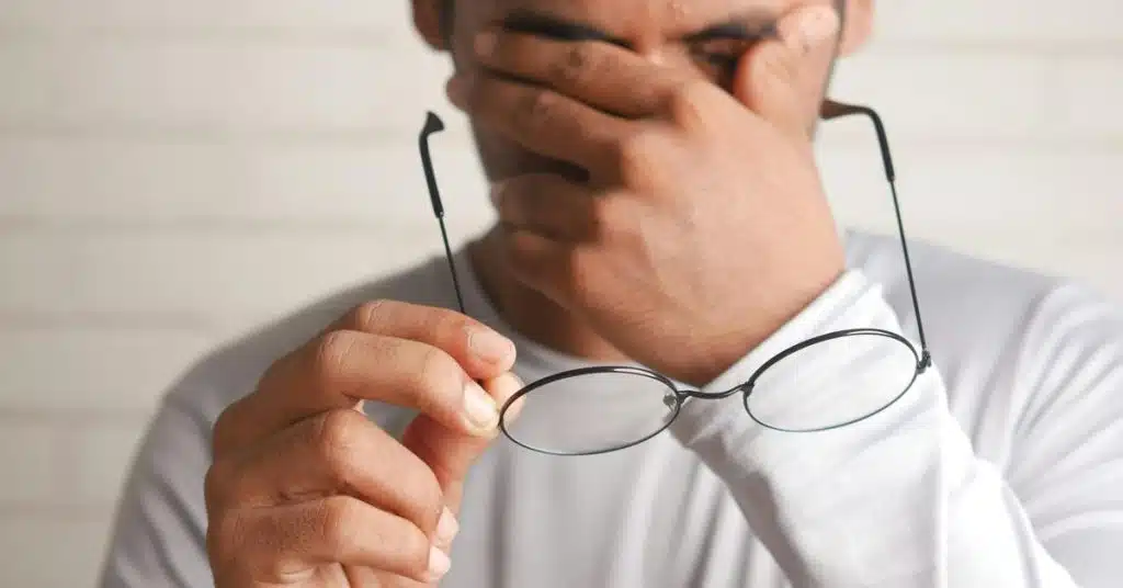A person holding eyeglasses while covering their face with one hand.