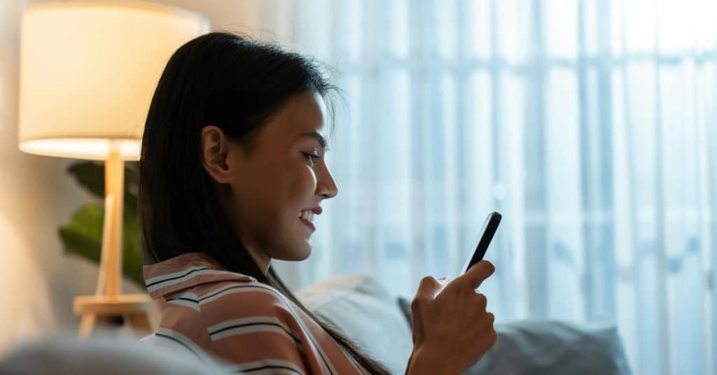 A woman smiling while looking at her phone on a couch.