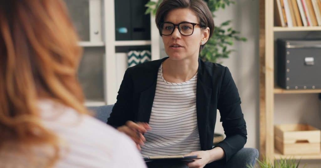 A woman wearing glasses speaking to another person in an office setting.