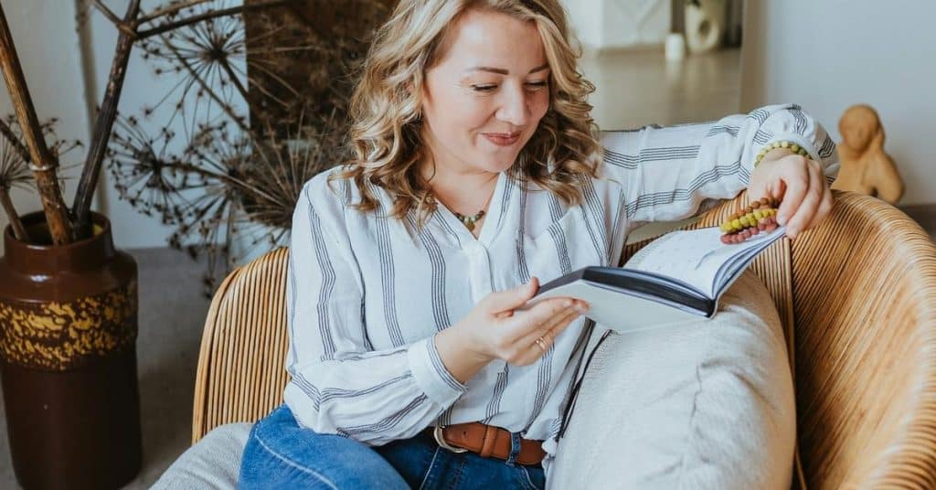 A woman smiling while reading a book in a cozy chair.
