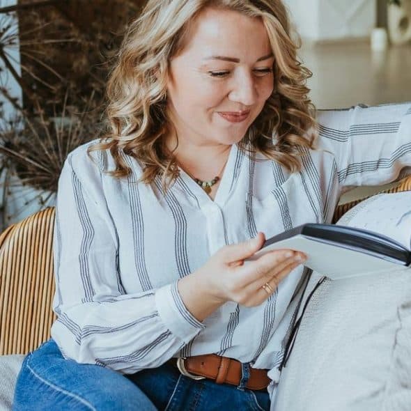 A woman smiling while reading a book in a cozy chair.