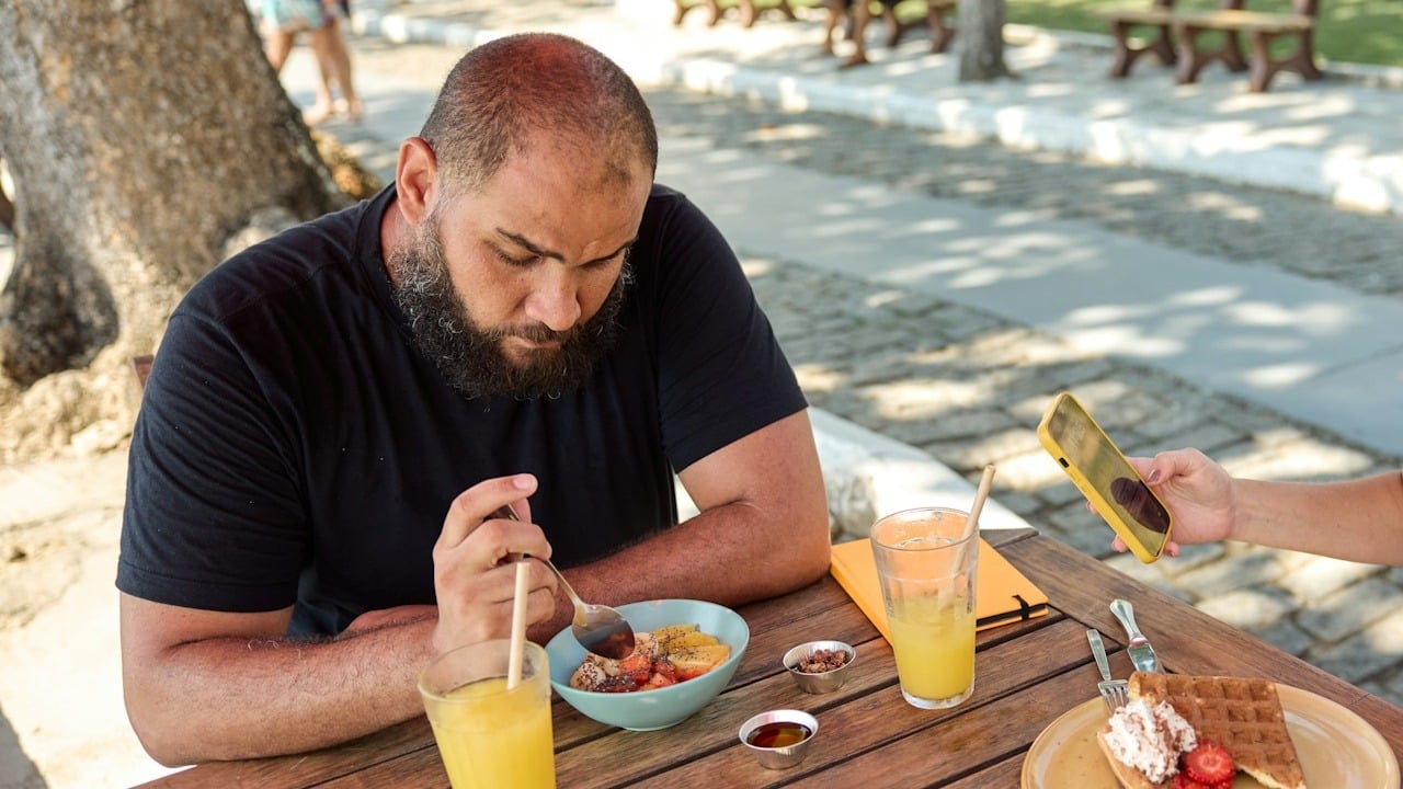 A bearded man sitting at a table having some snacks.