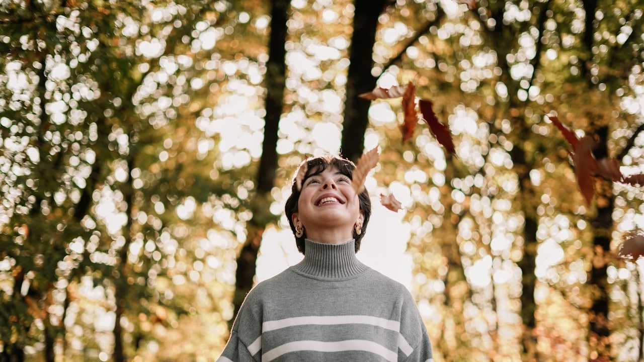 A person in a striped sweater throwing leaves in the air.