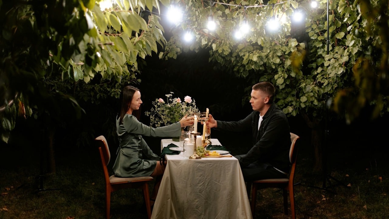 A man and woman share a romantic candlelit dinner at a small table outdoors.