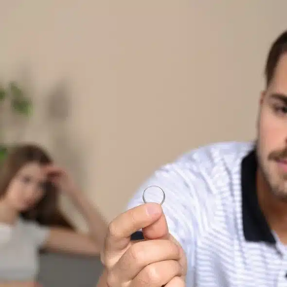 A man in a striped shirt holds a silver ring while a woman sits blurred behind.