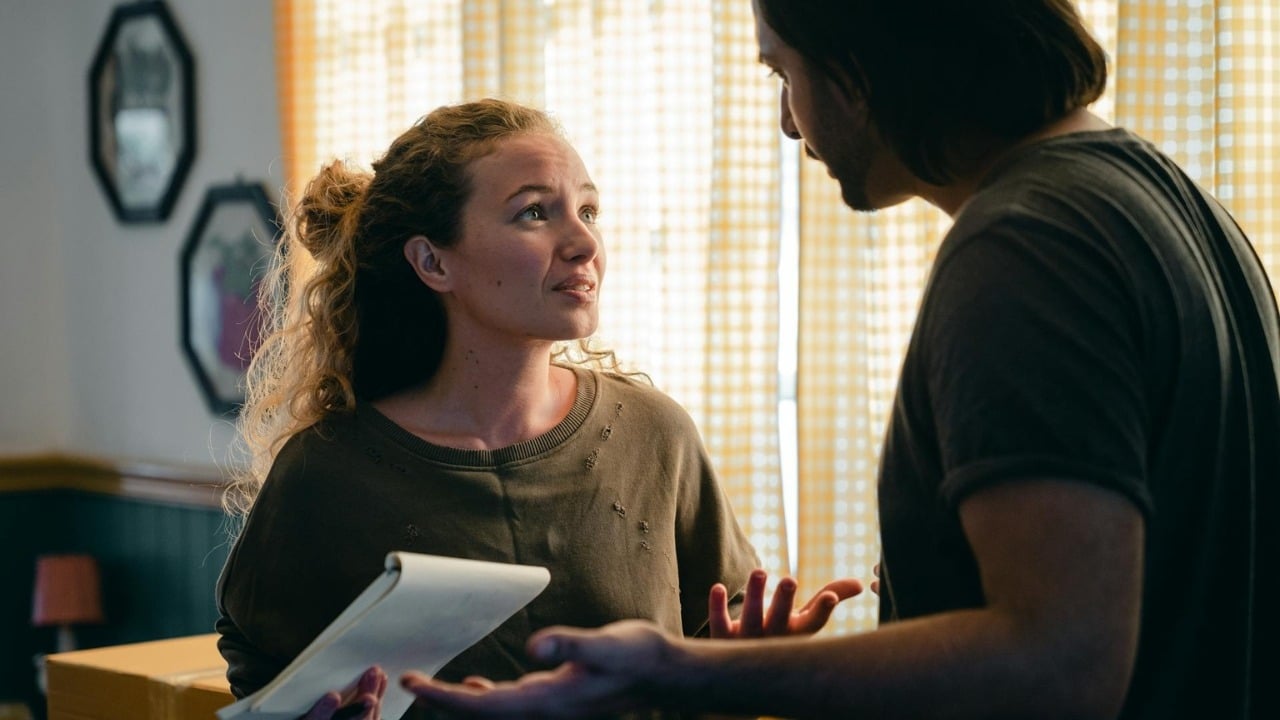 A woman holding a notebook looks up at a man gesturing with his hands during conversation.
