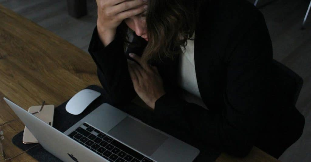 A stressed person holding their head while working on a laptop.