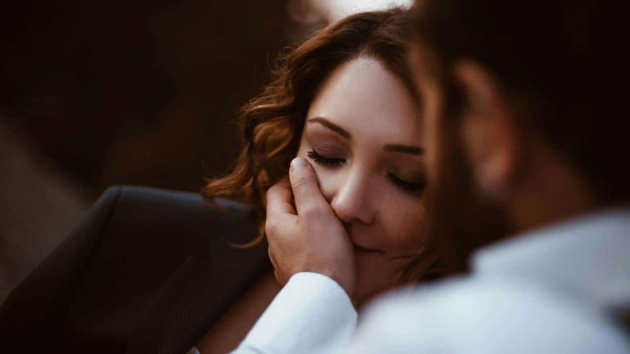 Close-up of a hand gently cupping a woman's face while her eyes are closed softly.