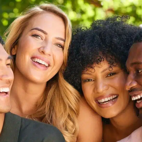 Four smiling people of various ethnicities lean their heads together against a leafy green background.
