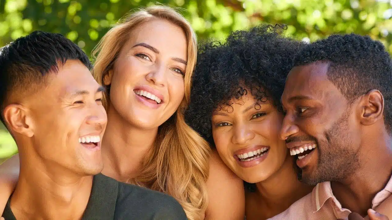 Four smiling people of various ethnicities lean their heads together against a leafy green background.